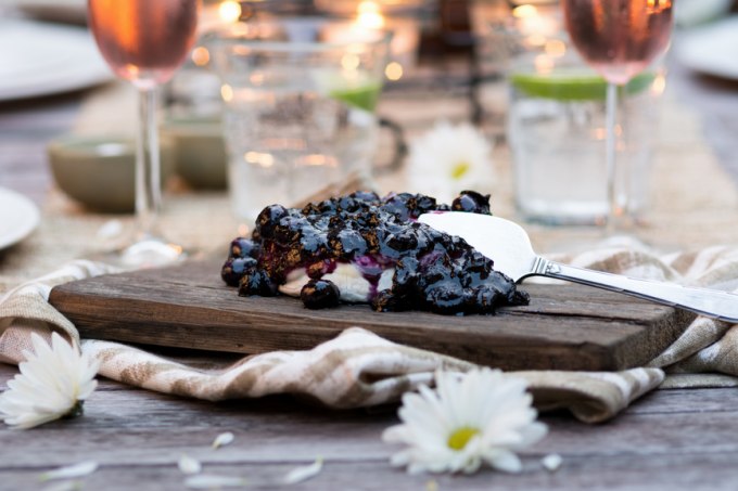 A picture of a spoon with blueberry compote that is topped on cheese on a cheese tray.