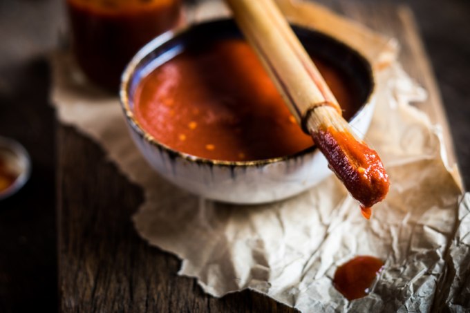 A close up of a bowl filled with BBQ sauce with a brush sitting on top of aluminum foil for grilling