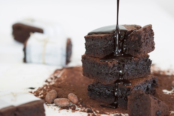 A stack of square brownies with a dark chocolate sauce being poured over top