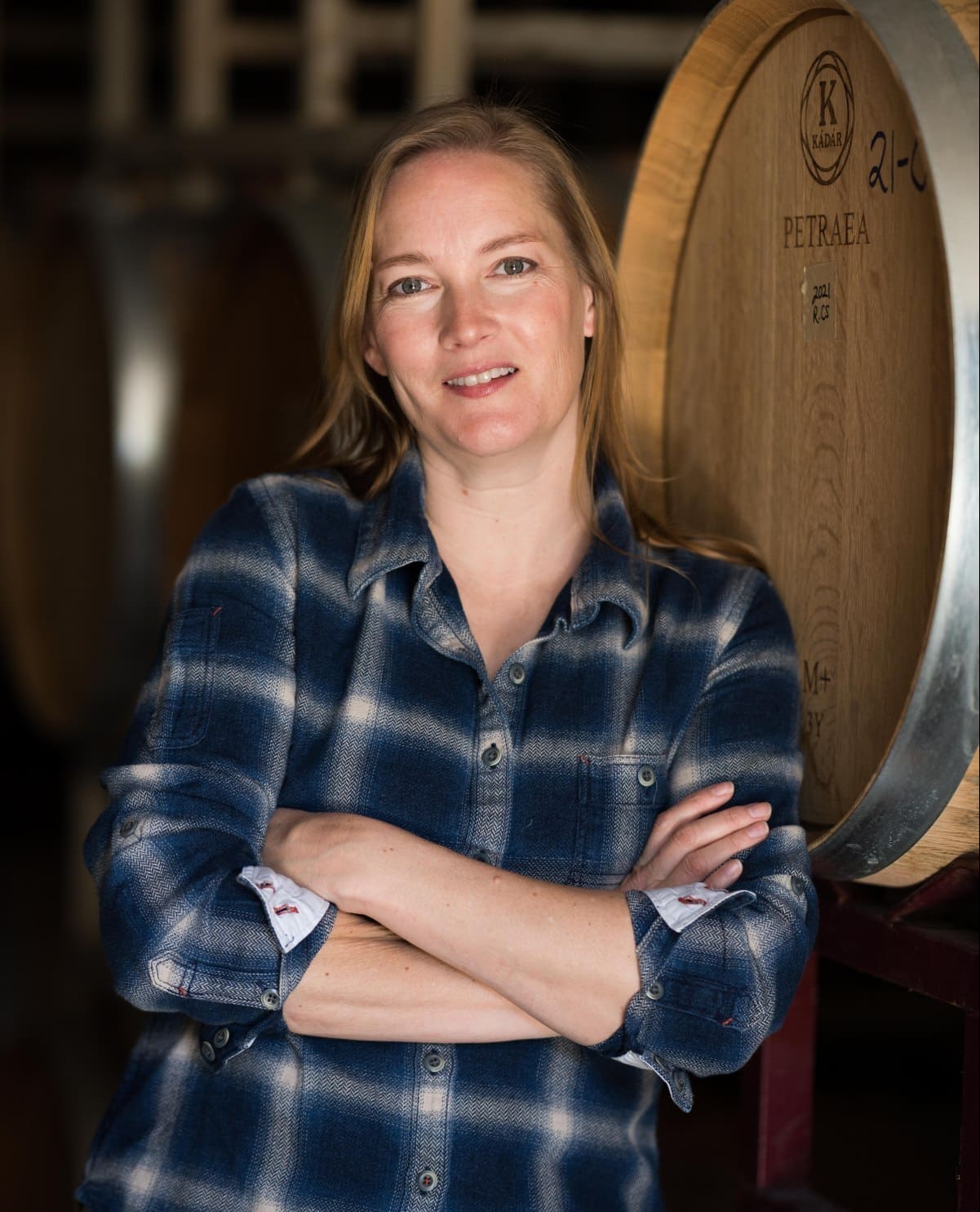 RM winemaker Meredith Sarboraria is wearing a blue plaid shirt and smiling next to a barrel in the cellar