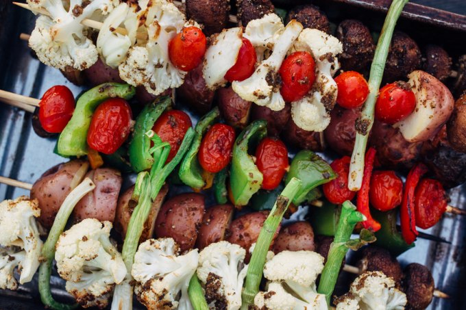 Cherry tomatoes, cut up portobello mushrooms, cut up green bell peppers threaded on bamboo skewers sitting on a tray ready to be grilled.