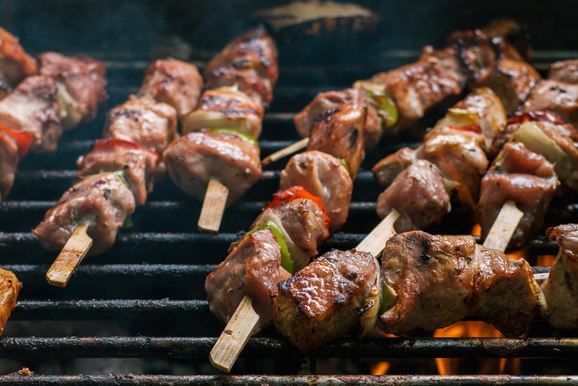 Skewers with steak pieces, cut up bell peppers on top of a flaming grill