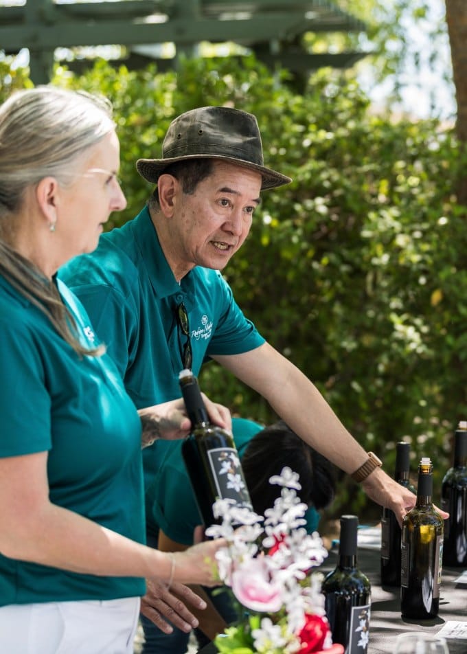  staff are wearing turquoise polos and pouring red wine to guests at a table in the garden during a club event