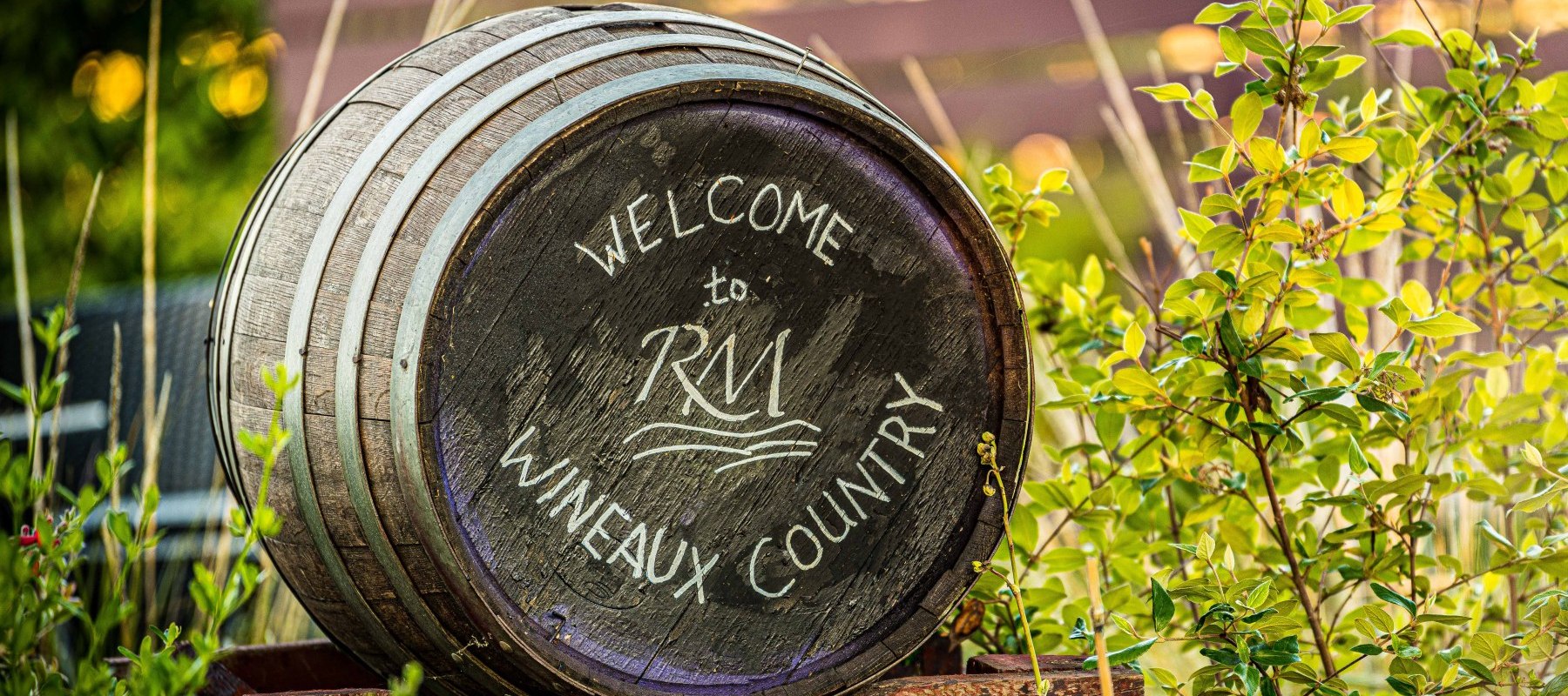 A close up of an old barrel in the tasting room garden that says “Welcome to Wineaux Country.”